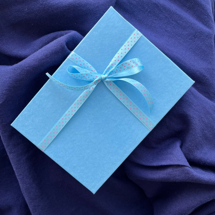 Photograph of a pale blue gift box tied with a blue and pink polka dot ribbon, sitting on navy blue linen.