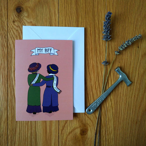 Photo of a greetings card depicting two suffragettes arm in arm from behind, one with a 