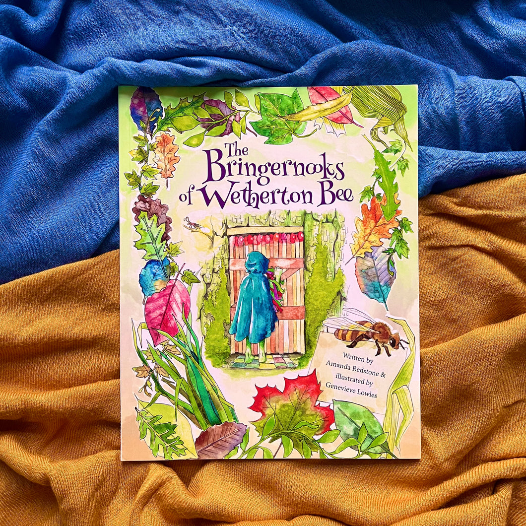 Photo of a book titled “The Bringernooks of Wetherton Bee” The cover illustration shows a figure wearing a blue cloak and hood facing away and knocking on a wooden door in a stone wall. Around the borders are leaves of various colours. In the corner, the caption reads “Written by Amanda Redstone & illustrated by Genevieve Lowles”.