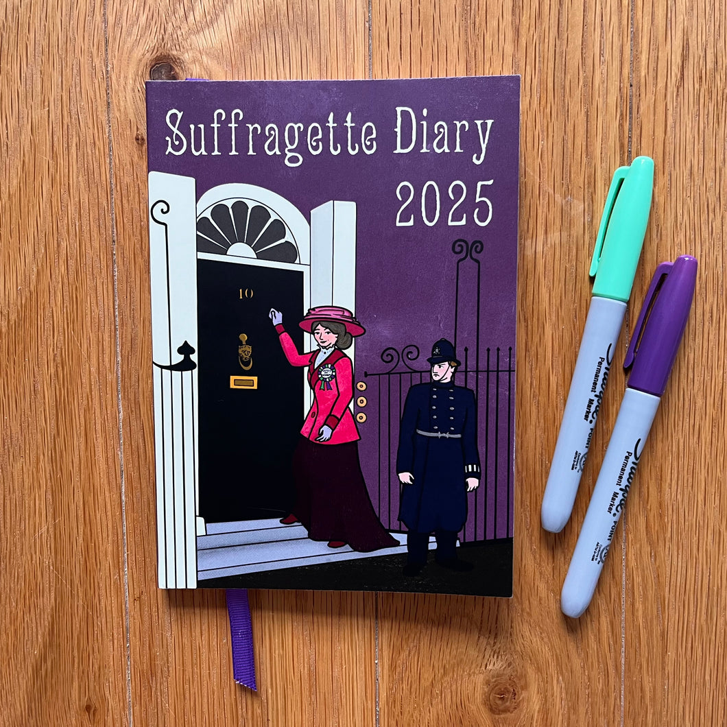Photo of the purple Suffragette Diary 2025. Below the title, a suffragette in red knocks at the door of 10 Downing Street while smirking. A policeman watches, glowering. Next to the diary are purple and green felt tip pens.