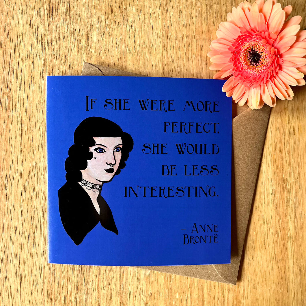 Photo of a blue greetings card next to a peach flower. The card depicts the quote 'If she were more perfect, she would be less interesting' by Anne Bronte, with a portrait of her as a Goth.
