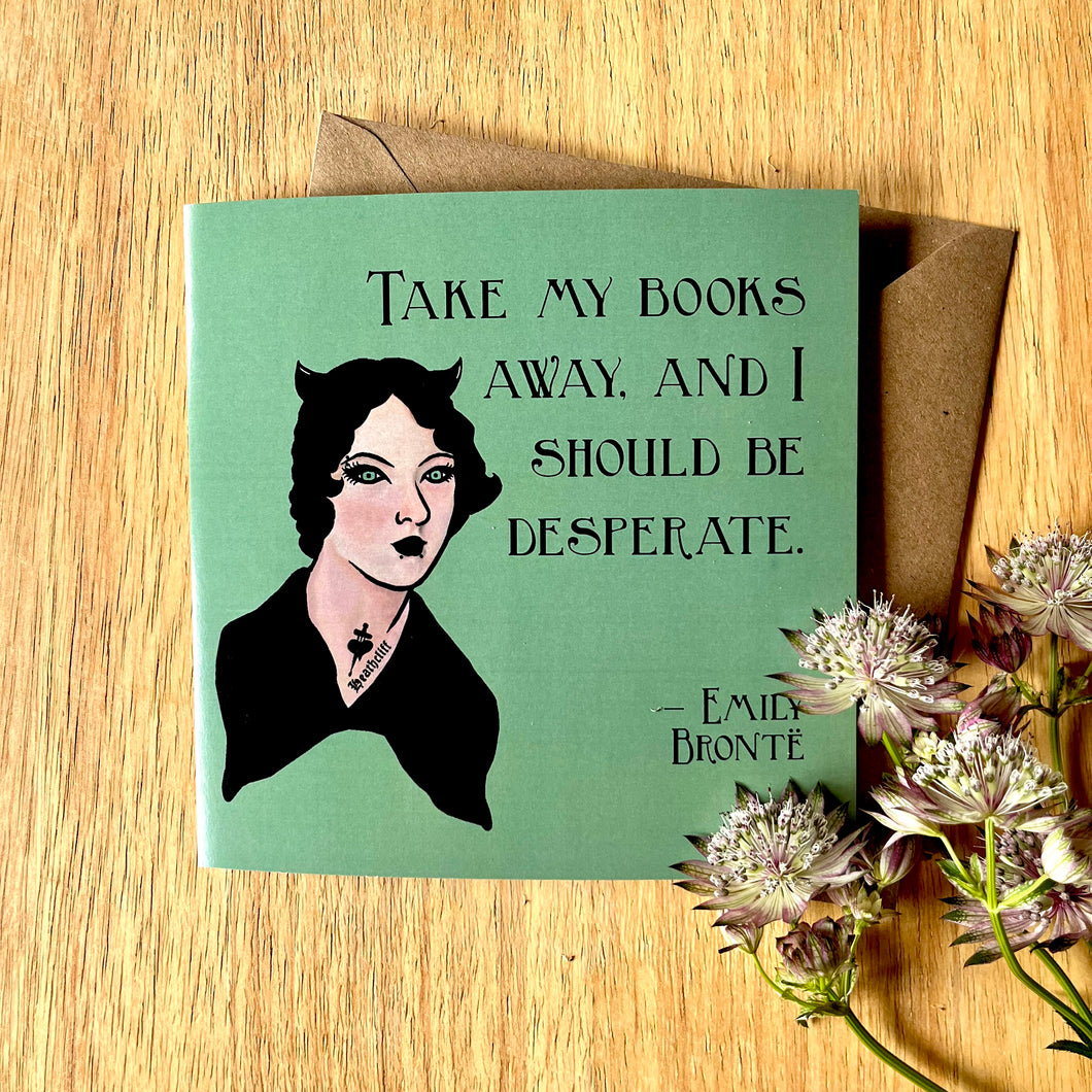 Photo of a green greetings card next to a mauve & white flower. The card depicts the quote 'Take my books away, and I should be desperate' by Emily Bronte, with a portrait of her as a Goth.
