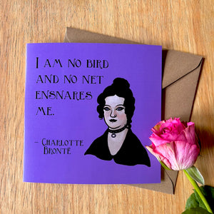 Photo of a purple greetings card next to a pink rose. The card depicts the quote 'I am no bird and no net ensnares me' by Charlotte Bronte, with a portrait of her as a Goth.