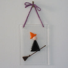 Load image into Gallery viewer, Photo of glasswork which depicts a witch in a minimalist style, with a black dress and orange hat, flying on a broomstick. The artwork hands from a purple thread.