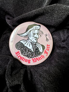 Photo of a pocket mirror, with a brown background and black-and-white mediaeval woodcut artwork of stereotypical crone with warts and a large nose. The caption reads 'Resting Witch Face' in a red Gothic typeface. Positioned on black fabric.