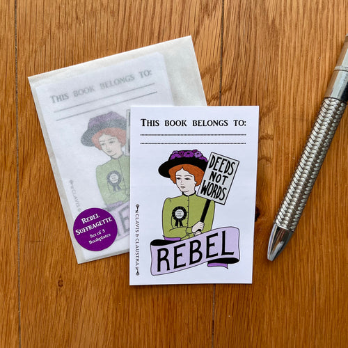 Photograph of a rectangular sticker featuring a suffragette with red hair and a green outfit wearing a rosette and holding a placard reading “Votes For Women”. Below her is a banner reading “Rebel and above other words “This book belongs to:…” – with room to write your name. Also in the photo is a packet of these bookplate stickers and a silver pen.