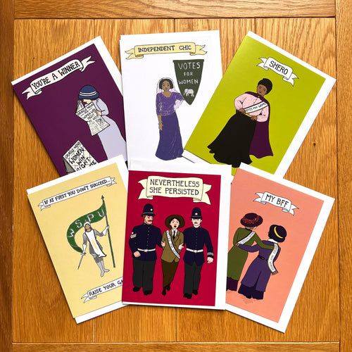 Photo of six suffragette-themed cards, each with a unique colour and design along with a white envelope. Included are the BBF card, Shero card, You’re A Winner card, Nevertheless She Persisted card, Raise Your Game card, and Independent Chic card.