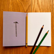 Load image into Gallery viewer, Photo of inside a notebook, which shows a blank page of dotted paper with three pencils on top. The inside cover features a toffee hammer.