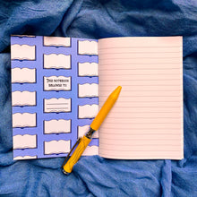Load image into Gallery viewer, Photo of the inside of the notebook, with lined paper on the right. The inside cover is blue with a repeating pattern of open books, one of which says “This Notebook Belongs To:” with a space for writing. A yellow pen lays on the book.
