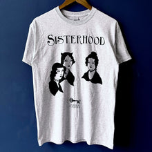 Load image into Gallery viewer, Photo of the t-shirt hanging up from a hanger against a blue background.