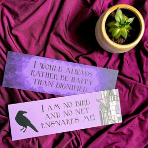 Photo of 2 bookmarks laid out next to a tiny plant. The purple bookmarks sit on a purple fabric and feature quotes from Jane Eyre, with images of a ruin and a crow.