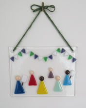 Load image into Gallery viewer, Photo of the glass artwork, which features six women in a minimalist style holding placards and underneath some bunting in suffragette colours. The glass artwork hangs from some green string on a wall.