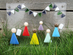 Photo of the glass artwork, which features six women in a minimalist style holding placards and underneath some bunting in suffragette colours. The glass artwork features two holes at the top corners for mounting, and has been propped up outside against a wall in the grass.