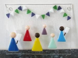 Photo of the glass artwork, which features six women in a minimalist style holding placards and underneath some bunting in suffragette colours. The glass artwork features two holes at the top corners for mounting and has been propped up against the wall.