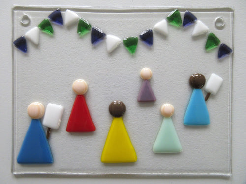 Photo of the glass artwork, which features six women in a minimalist style holding placards and underneath some bunting in suffragette colours. The glass artwork features two holes at the top corners for mounting.