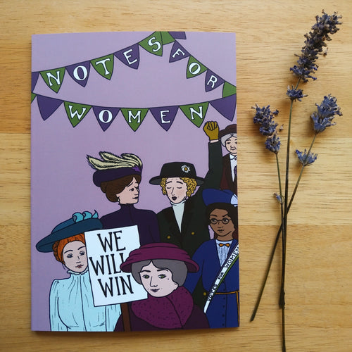 Photo of the notebook, with “Notes For Women” written in bunting, with an assortment of suffragettes parading in the foreground wearing hats and sashes. One holds their fist in the air. Another holds a sign that says “We Will Win”. Next to the notebook are some sprigs of lavender.