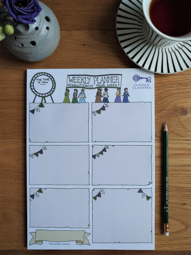 Photo of the planner. At the top is “Weekly Banner” and “Revolutionize your week!” in a banner held aloft by seven suffragettes, next to a large rosette that says “The time is now”. In the top-right is the Clavis & Claustra key logo. Beneath, the page is segmented into different days, each titled by suffragette bunting. The bottom left has a distinct blank banner titled “This week’s mission”. Next to the pad is a pencil, small vase with flowers, and cup of black tea on a saucer.