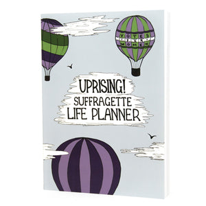 Photo of the light blue planner, which shows three hot air balloons in suffragette colours in the sky with the title “Uprising! Suffragette Life Planner” as text within a cloud.