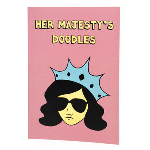 Photo of Her Majesty’s Doodles notebook, featuring a pink cover with the title in yellow and a stylised illustration of an unsmiling woman with long black hair, wearing sunglasses and an extravagant blue crown.