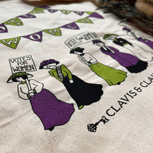 Load image into Gallery viewer, An oblique image of the bag close up, showing suffragettes marching under purple and green bunting and carrying banners. The Clavis and Claustra logo is visible at the bottom of the image.