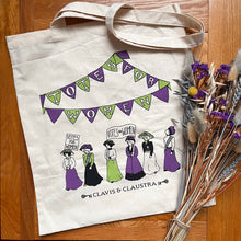 Load image into Gallery viewer, Large cotton tote bag, pictured with a sprig of purple and pale blue dried flowers. The bag features an illustration of suffragettes marching under purple and green bunting with lettering spelling: Totes For Women. The suffragettes are carrying banners reading: Votes For Women. 