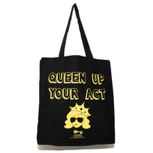 Load image into Gallery viewer, Photo of a black tote bag. The bag says “Queen Up Your Act” in yellow outline letters and features the image of an unsmiling woman with long hair wearing sunglasses and a crown. The handles are up in the air.