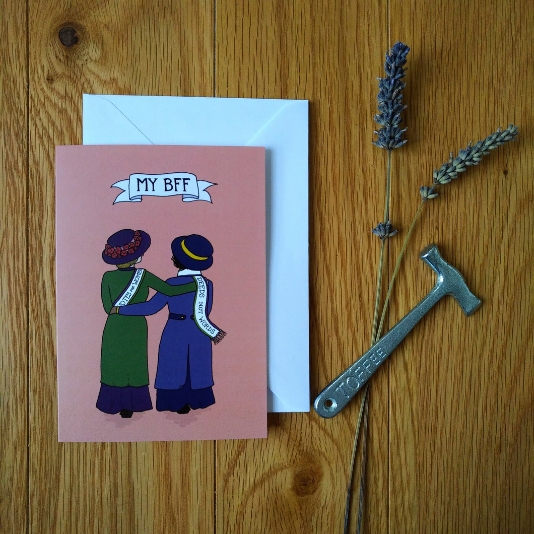 Photo of a greetings card depicting two suffragettes arm in arm from behind, one with a 