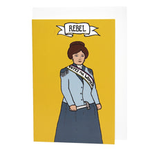 Load image into Gallery viewer, Photo of a mustard-coloured card laid on a white envelope on a table. The card shows a suffragette in a blue blazer and darker blue skit. She wears a sash that says “Votes For Women” and holds a toffee hammer in her hand. The banner at the top reads “Rebel”.