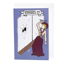 Load image into Gallery viewer, Photo of a purple greetings card. The image shows a suffragette wearing a “Votes For Women” sash and red hat wielding a toffee hammer. She stands next to a large window with a giant break in the middle and cracks emerging from the centre. Broken glass is on the floor. The banner caption reads “Smashed It!”.
