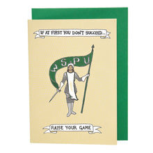 Load image into Gallery viewer, Photo of a pale card which shows a woman facing us who wears armour, white gloves, and a white smock and hat with pointed top. She holds a sword in her right and a flowing green flag in her left which reads “W.S.P.U”. Above and below the woman on a banner are the words “If at first you don’t succeed… Raise your game.” The card is on top of a green envelope.