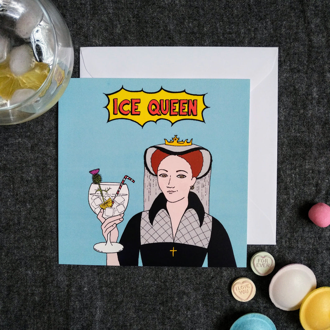 Photo of a light blue card featuring Mary Queen of Scots smirking and toasting with a large cocktail in a glass, with ice, lemon, a straw, and a flower. The caption reads “Ice Queen” in red text inside a yellow exploding bubble. Next to the card are some sweets and a drink with ice.