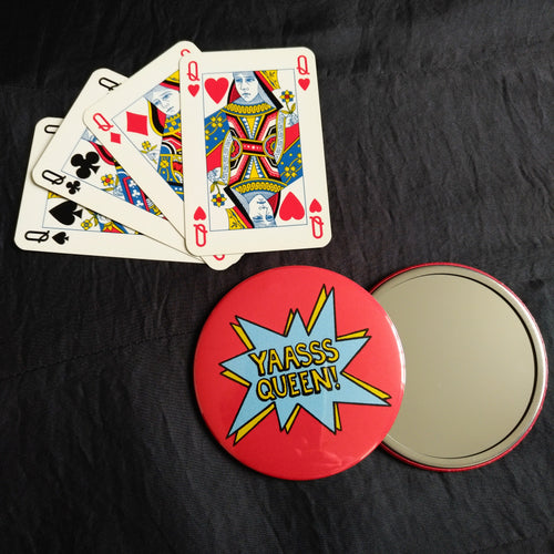 Photo of two mirrors, showing each side. The back of the mirror is all in red with “YAASSS Queen” in yellow text within a blue exploding bubble accented with yellow. Next to the mirror is four playing cards, showing the queens of each suit.