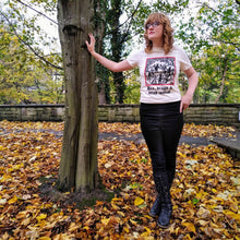 Load image into Gallery viewer, Photo of a white woman outside with one hand against a tree. She wears black boots and trousers and a t-shirt featuring a mediaeval woodcut artwork depicting witches and demons joining hands and dancing in a circle, framed by a thin red border. Beneath it the caption reads &#39;Hex, drugs &amp; mind control&#39;. Autumn leaves carpet the ground.