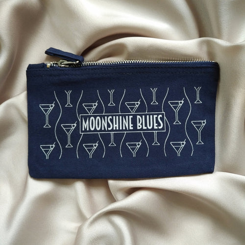 Photo of the bag, a dark blue fabric pouch with a silver zip at the top. The design on the side shows a pattern of martini glasses in silver, with a caption in the centre that says “Moonshine Blues”.