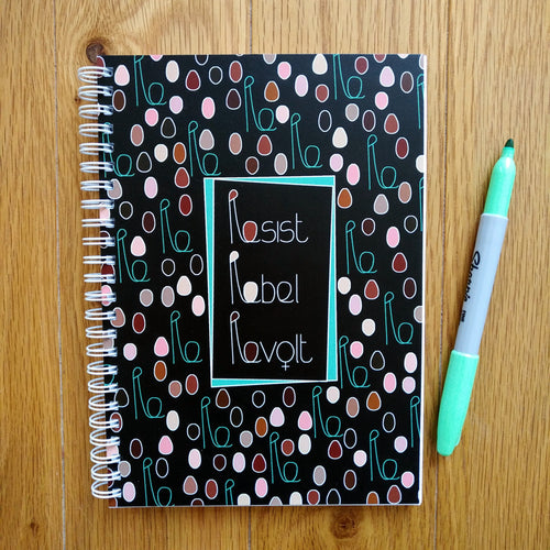 A black spiral-bound notebook with minimalist figures of different colours and sizes representing a crowd of women with their fists upraised. The combined head and raised fist resembles the letter “R”, which is used in the caption. In the centre is a black rectangle outlined in green with the words “Resist” and “Rebel” and “Revolt” in white. Next to the card is a green pen.