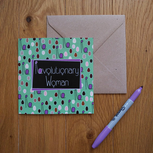 A light turquoise card with minimalist figures of different colours and sizes representing a crowd of women with their fists upraised. The combined head and raised fist resembles the letter “R”, which is used in the caption. In the centre is a black rectangle outlined in purple with the words “Revolutionary Women” in white. The “o”s in the words are turned into feminine symbols. Next to the card is a brown envelope and a purple pen.