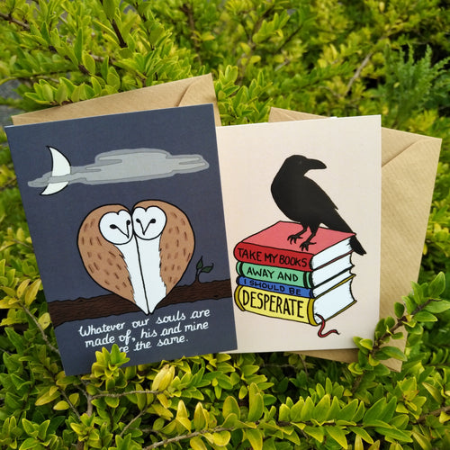 Photo of both quotelets resting on brown envelopes against the branches of a bush. The left quotelet shows a dark night and two owls pressed against each other in a way that resembles a heart. The caption reads “Whatever our souls are made of, his and mine are the same”. The right quotelet has a light background. In the foreground, a raven stands on a stack of three hardback books. The spines of these books line up to read “Take My Books Away And I Should Be Desperate”.