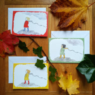 Three variants of the card, all with the same artwork in different colours: a girl in boots and a coat standing on the moors, as the wind blows through her hair. Behind her is the caption “No coward soul is mine - Emily Bronte.” There are variants in red and green and yellow. Next to the cards are some autumn leaves.