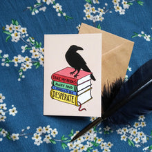 Load image into Gallery viewer, Photo of the quotelet, which has a light background. In the foreground, a raven stands on a stack of three hardback books. The spines of these books line up to read “Take My Books Away And I Should Be Desperate”. Next to the quotelet are a brown envelope and a black quill pen.