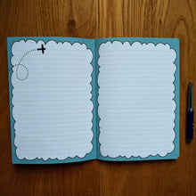 Load image into Gallery viewer, Photo of the open notebook, showing two blank lined pages fringes of light blue to resemble clouds. An illustration of a plane with a trail that shows it has just performed a loop is on the top left of the left page. A pen has been placed next to the notebook.