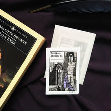 Load image into Gallery viewer, Photo of the Jane Eyre bookplate, which illustrates gothic windows and stairs and “I am no bird and no net ensnares me” carved into the wall. A raven sits on a broken pillar. In the top left is a space to write starting with “This Book Belongs To…”. The bookplate is pictured next to the Penguin Classics edition of Jane Eyre.
