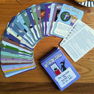 Aerial photo of the Suffra-Greats! Card game. The shows the title and “The card game for REBELS of all ages”. The illustration shows a suffragette wielding a hammer, ready to smash a glass display case containing a crown. The cards from the game are spread out in a fan. A plate with biscuits on is just in shot.