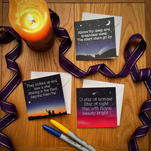 Load image into Gallery viewer, Photo of the Silent Stars, Star of Wonder, and Shining Stars Christmas cards, all laid out on individual white envelopes. A purple ribbon curls between them and two marker pens are nearby. The ribbon curls around a lit orange candle.