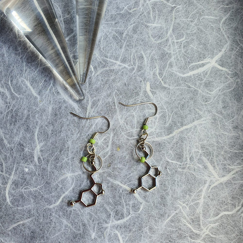 Photo of two earrings that feature hexagonal molecular effect shapes joined to lime green glass beads. Next to the earrings is the tip of a glass crystal.