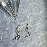 Photo of two earrings that feature hexagonal molecular effect shapes joined to lime green glass beads. Next to the earrings is the tip of a glass crystal.