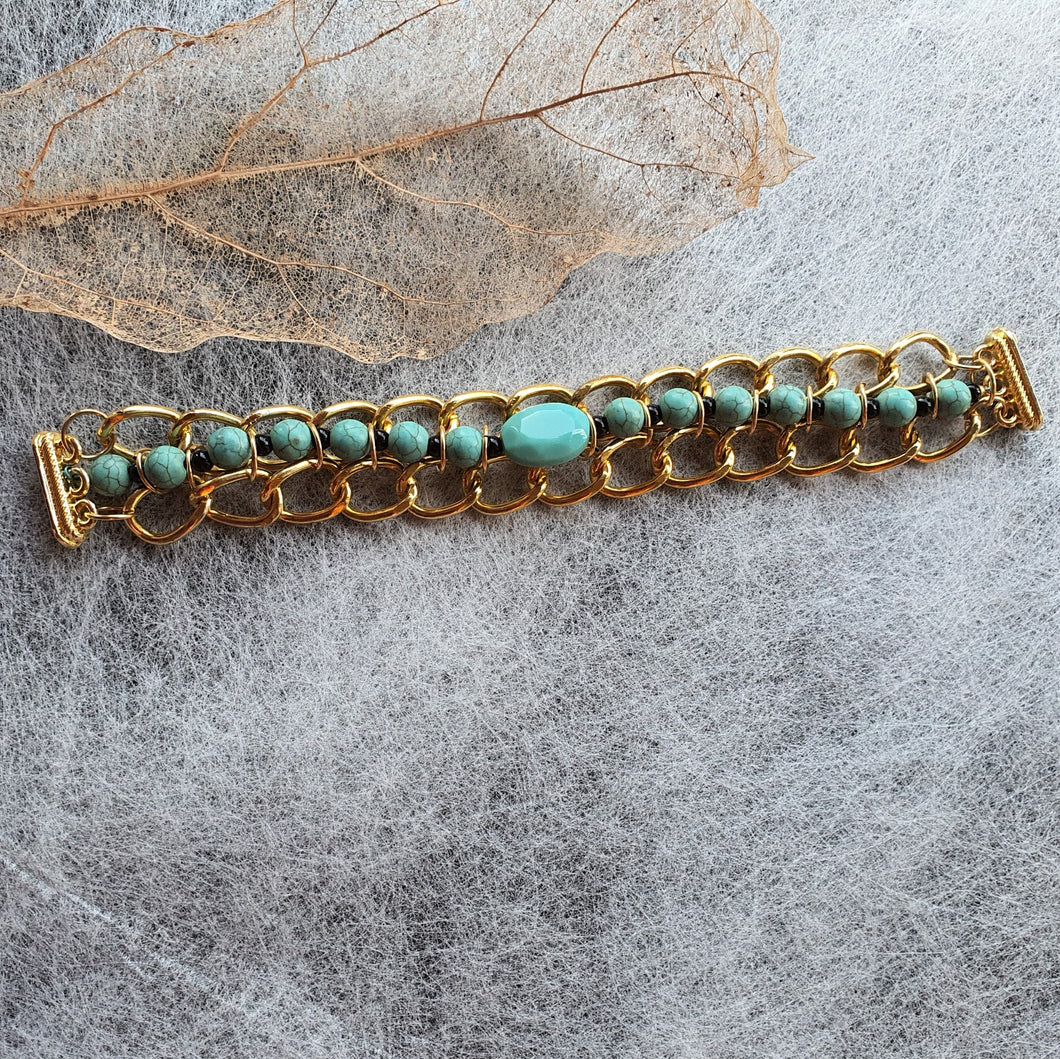 Photo of the bracelet, consisting of golden links that interweave with turquouise beads. The necklace is not joined and is laid flat.