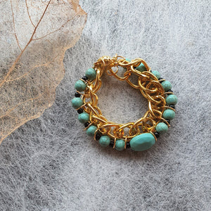 Photo of the bracelet, consisting of golden links that interweave with turquouise beads. The bracelet is clasped in a circle.