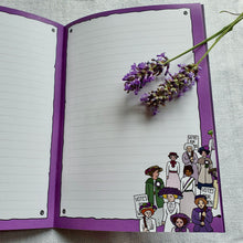 Load image into Gallery viewer, Photo from inside the notebook, with blank lined pages framed by purple colouring. In the bottom right corner is a parade of suffragettes wearing hats and sashes. On the notebook are some sprigs of lavender.