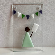 Photo of glass artwork, a rectangle that shows a suffragette in a minimalist style holding a sign beneath some white, green, and purple bunting. Two holes for hanging the artwork are in the top two corners.